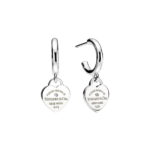 Two silver hoop earrings each with a heart charm engraved 'Please return to Tiffany & Co. New York 925' on a black background
