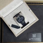 Watch with navy dial and metal case in a beige presentation box with a textured lining and a black strap. (Luxury timepiece)