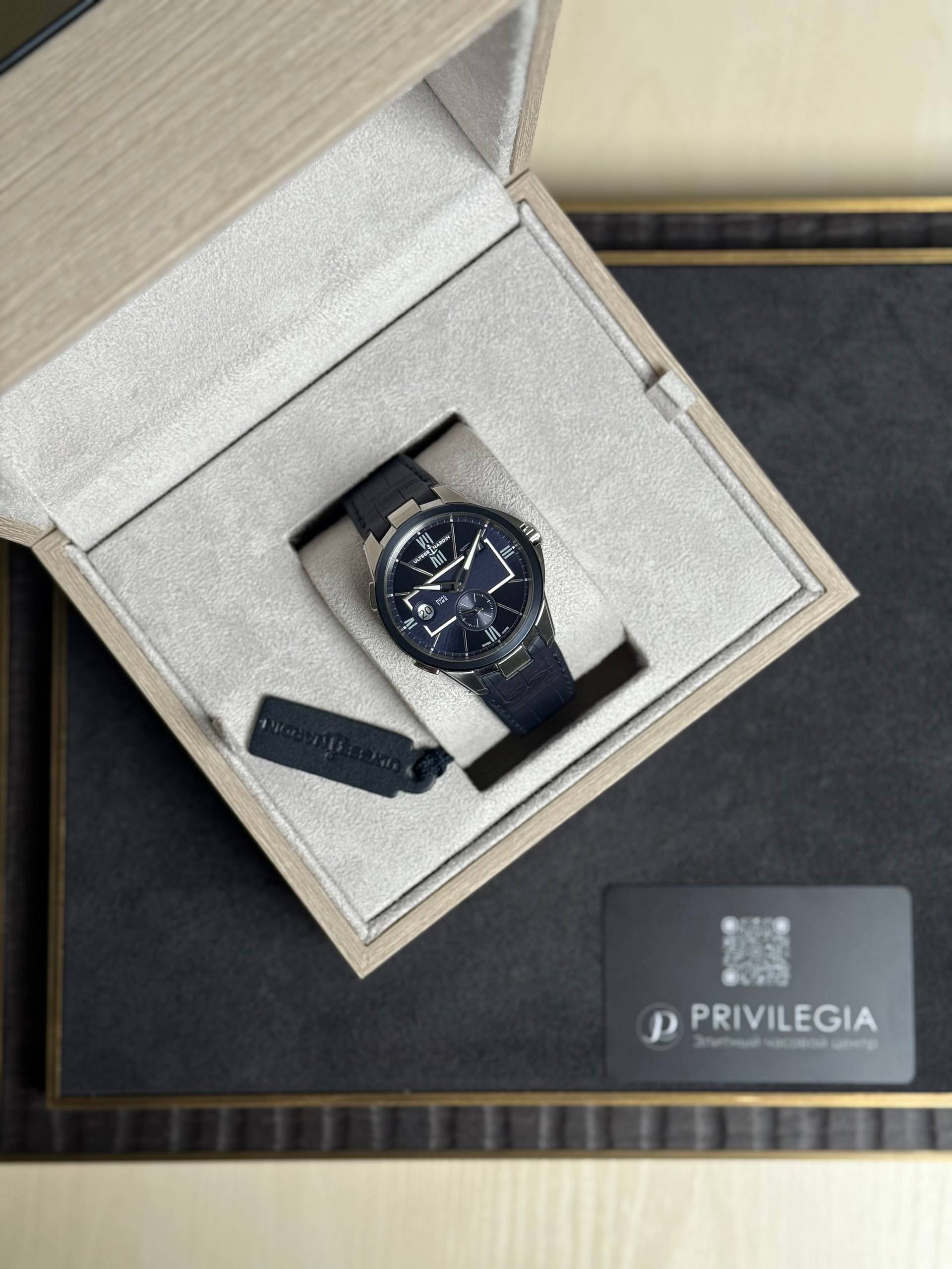 Watch with navy dial and metal case in a beige presentation box with a textured lining and a black strap. (Luxury timepiece)