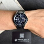 Close-up of a man's wrist wearing a blue dial luxury wristwatch with a metal band, showing Ulysse Nardin branding on the face.