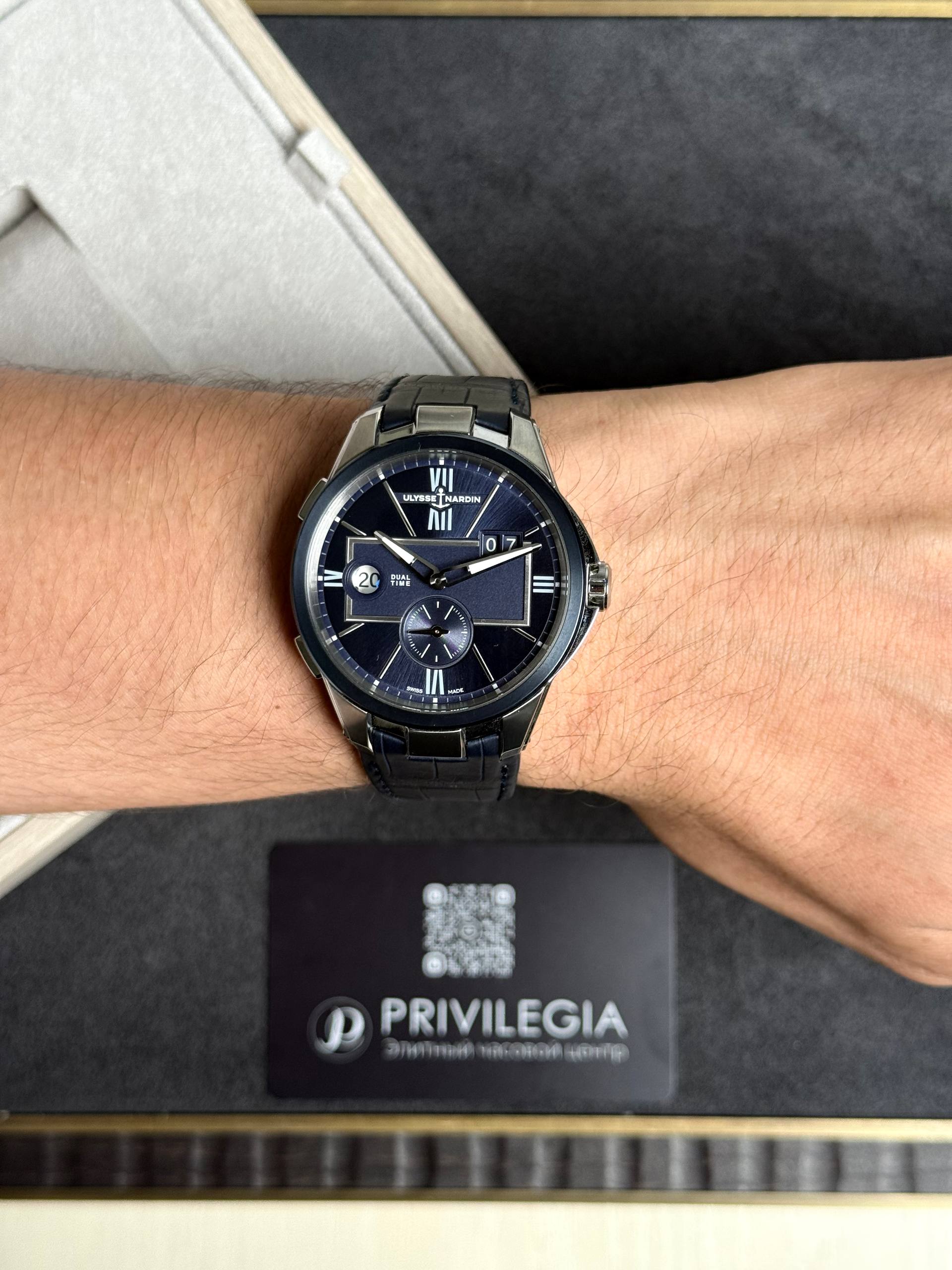 Close-up of a man's wrist wearing a blue dial luxury wristwatch with a metal band, showing Ulysse Nardin branding on the face.