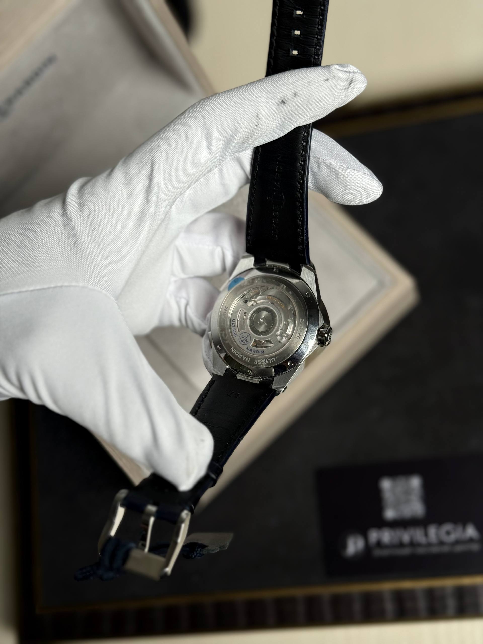 Back of a mechanical wristwatch with a visible rotor, held by a gloved hand in white gloves