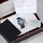 Ulysse Nardin watch with blue face in a brown presentation box, accompanied by manuals and a black leather wallet-like case.