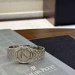 Diamond-encrusted silver wristwatch with metal bracelet on a branded display mat reading Audemars Piguet.