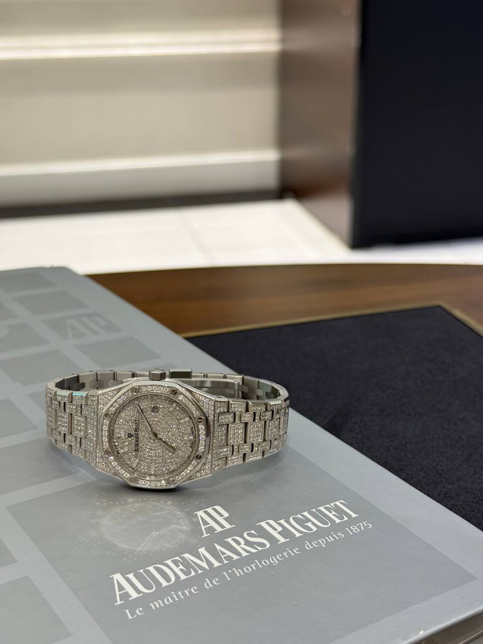 Diamond-encrusted silver wristwatch with metal bracelet on a branded display mat reading Audemars Piguet.