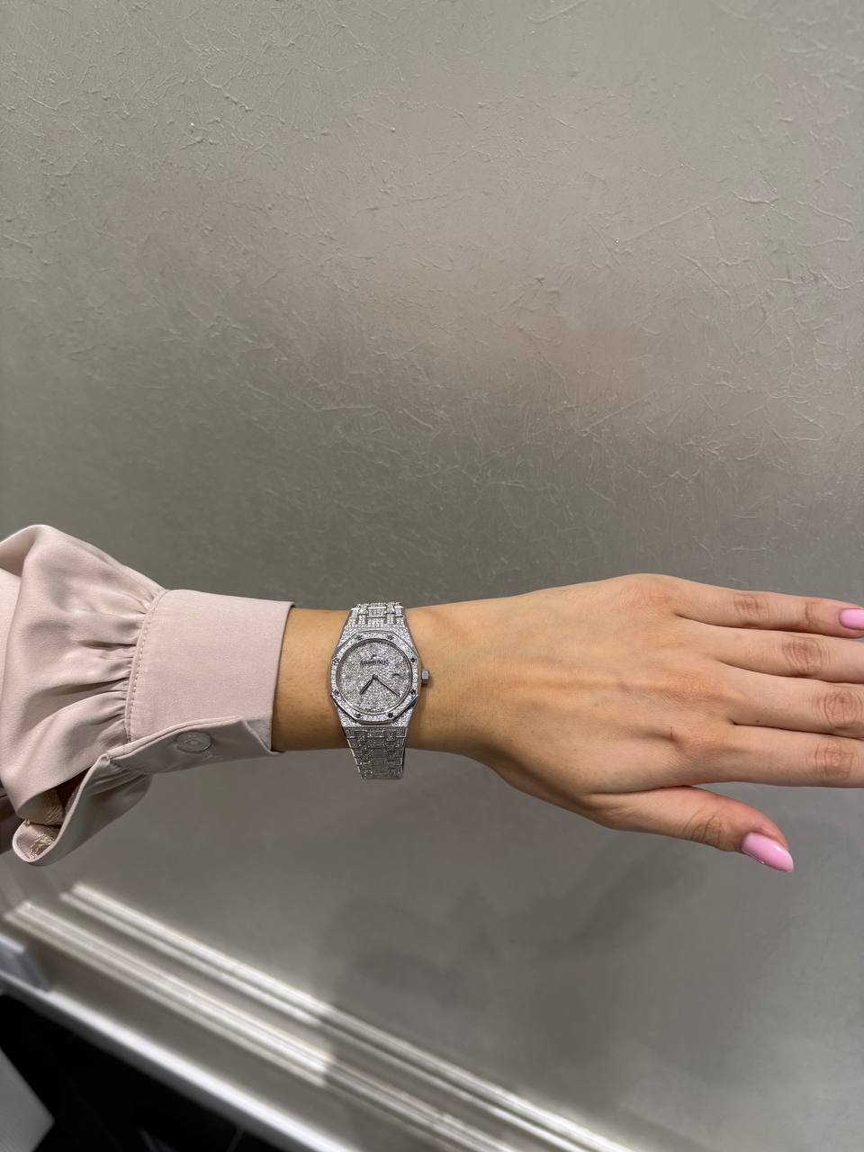 Wrist wearing a diamond-studded silver watch with a pale pink satin sleeve showing on the left arm.