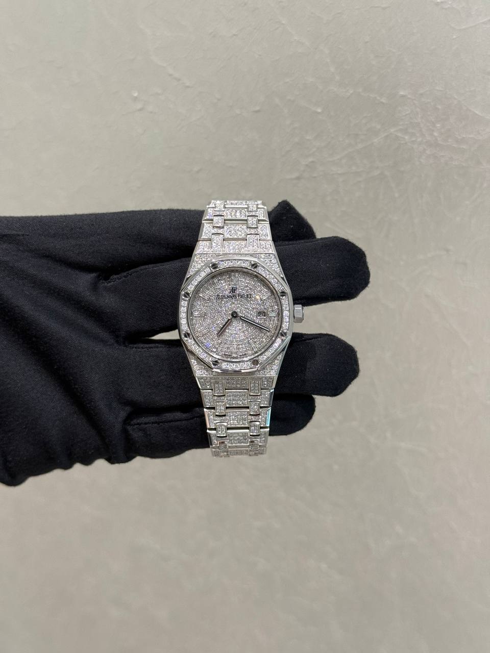 Diamond-encrusted wristwatch on a gloved hand, silver metallic band and sparkling dial.