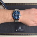 Breitling Superocean blue-dial wristwatch with stainless mesh band on the wrist, shown close-up on a dark background with a Privilegia card nearby.