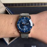 Blue Breitling SuperOcean automatic dive watch on a metal mesh bracelet worn on the wrist.