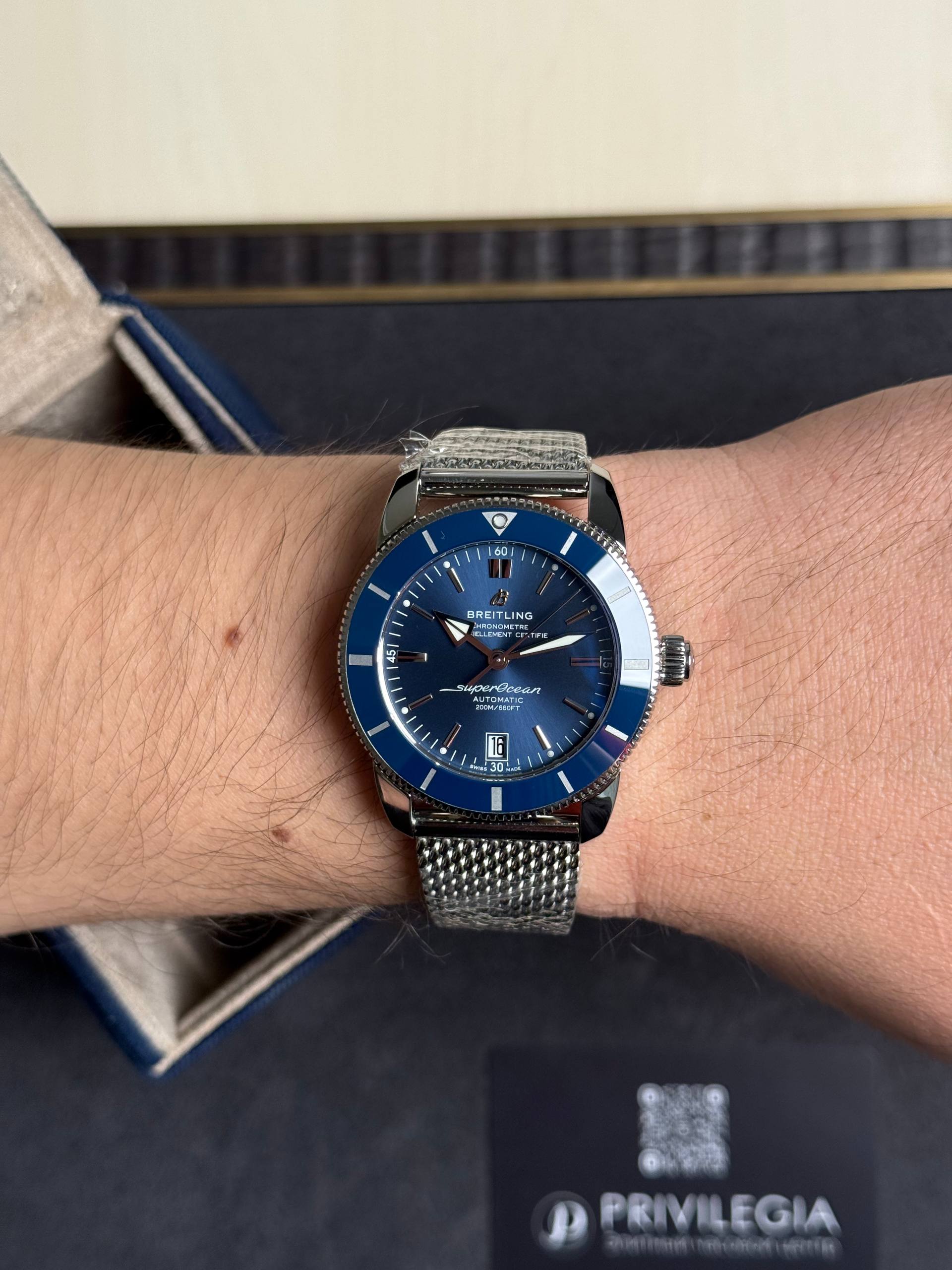Blue Breitling SuperOcean automatic dive watch on a metal mesh bracelet worn on the wrist.