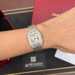 Diamond-studded Cartier wristwatch on a wrist with a pink Cartier box in the background