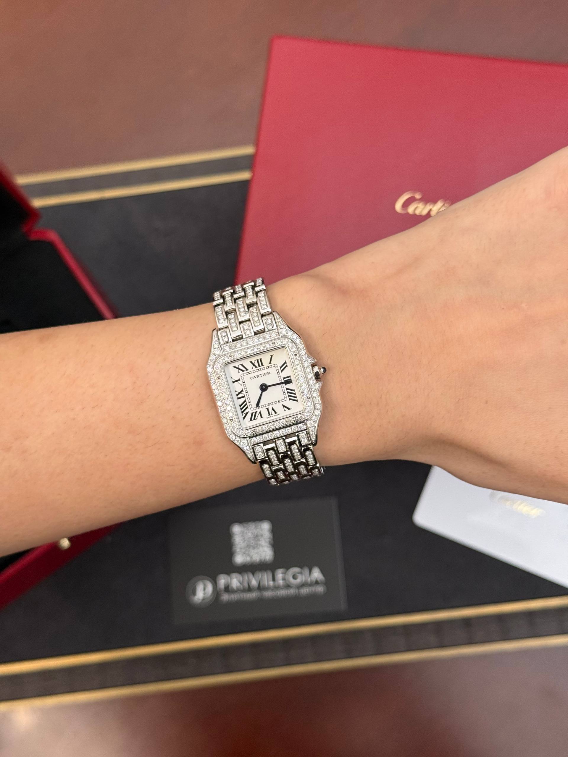 Diamond-studded Cartier wristwatch on a wrist with a pink Cartier box in the background