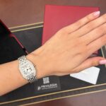 Diamond-encrusted rectangular wristwatch on a woman's wrist, pink manicure, with a red box in the background.