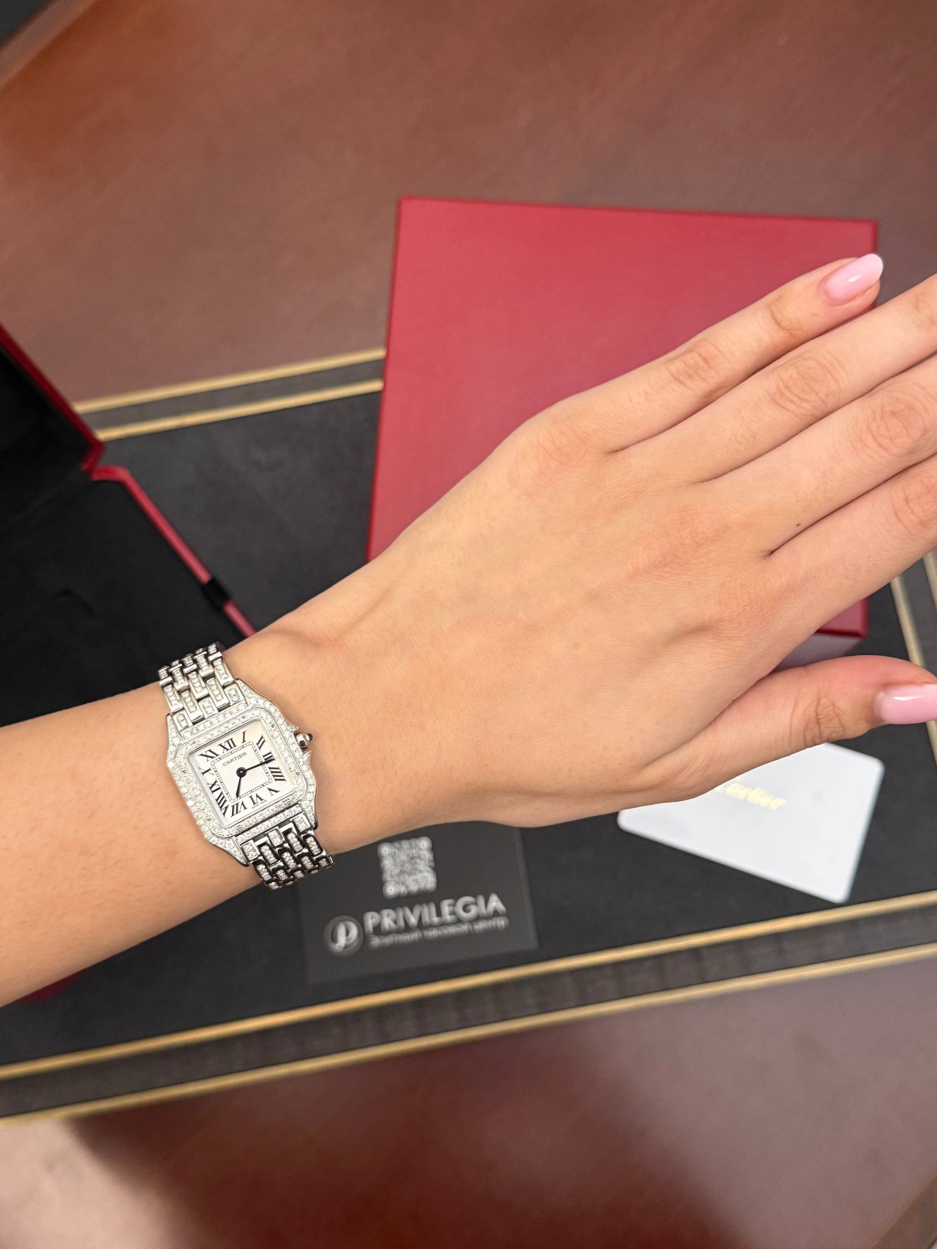 Diamond-encrusted rectangular wristwatch on a woman's wrist, pink manicure, with a red box in the background.