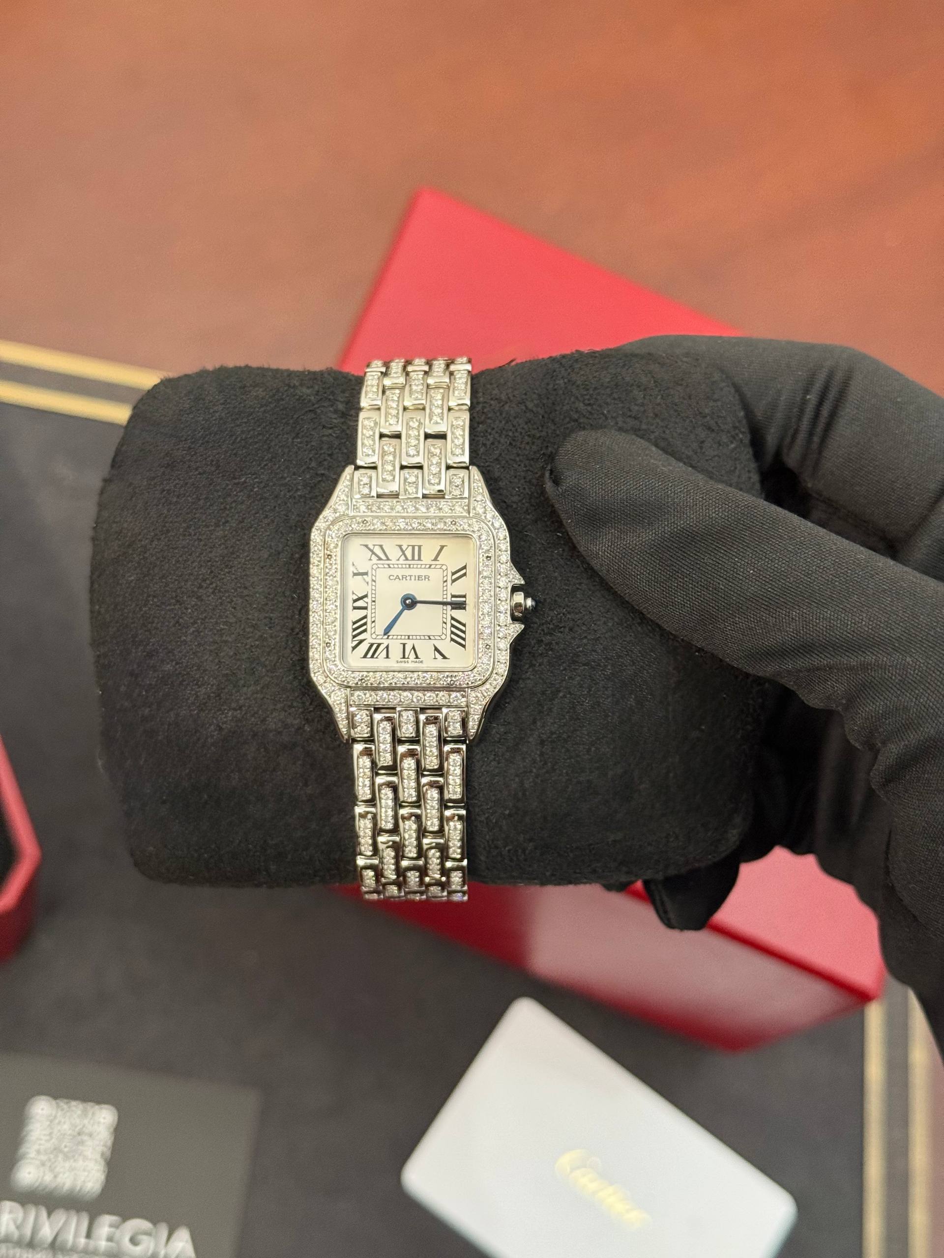 Diamond-encrusted silver Cartier wristwatch with Roman numerals on a white dial, resting on a black glove.