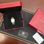 Luxury wristwatch displayed in an open red Cartier box with black interior lining and a metal link bracelet.