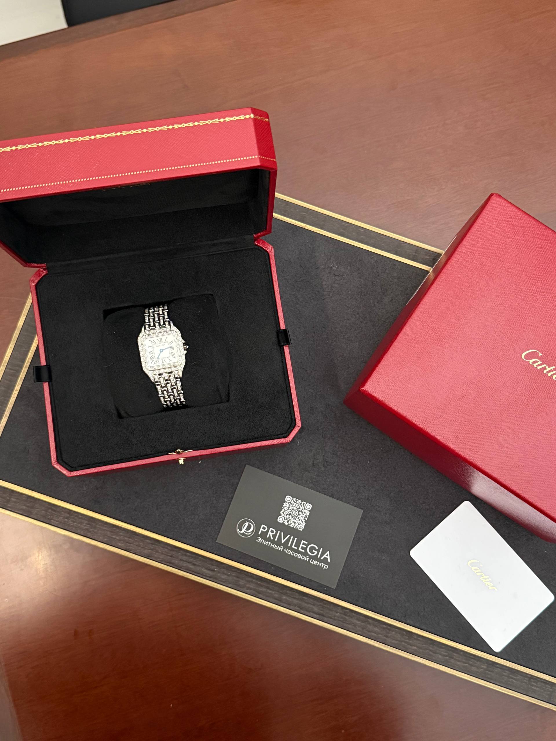 Luxury wristwatch displayed in an open red Cartier box with black interior lining and a metal link bracelet.