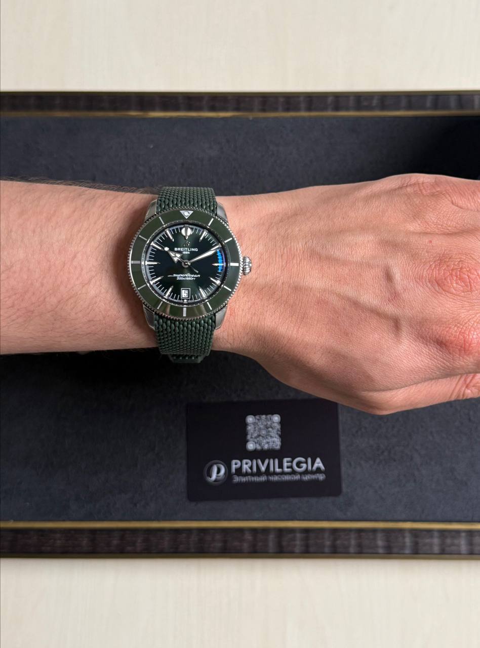 Breitling wristwatch with a dark dial and green fabric strap on a forearm resting on a black display box labeled Privilegia.