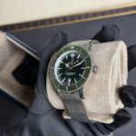 Close-up of a stainless steel Breitling Superocean wristwatch with a green bezel, held by gloved hand.