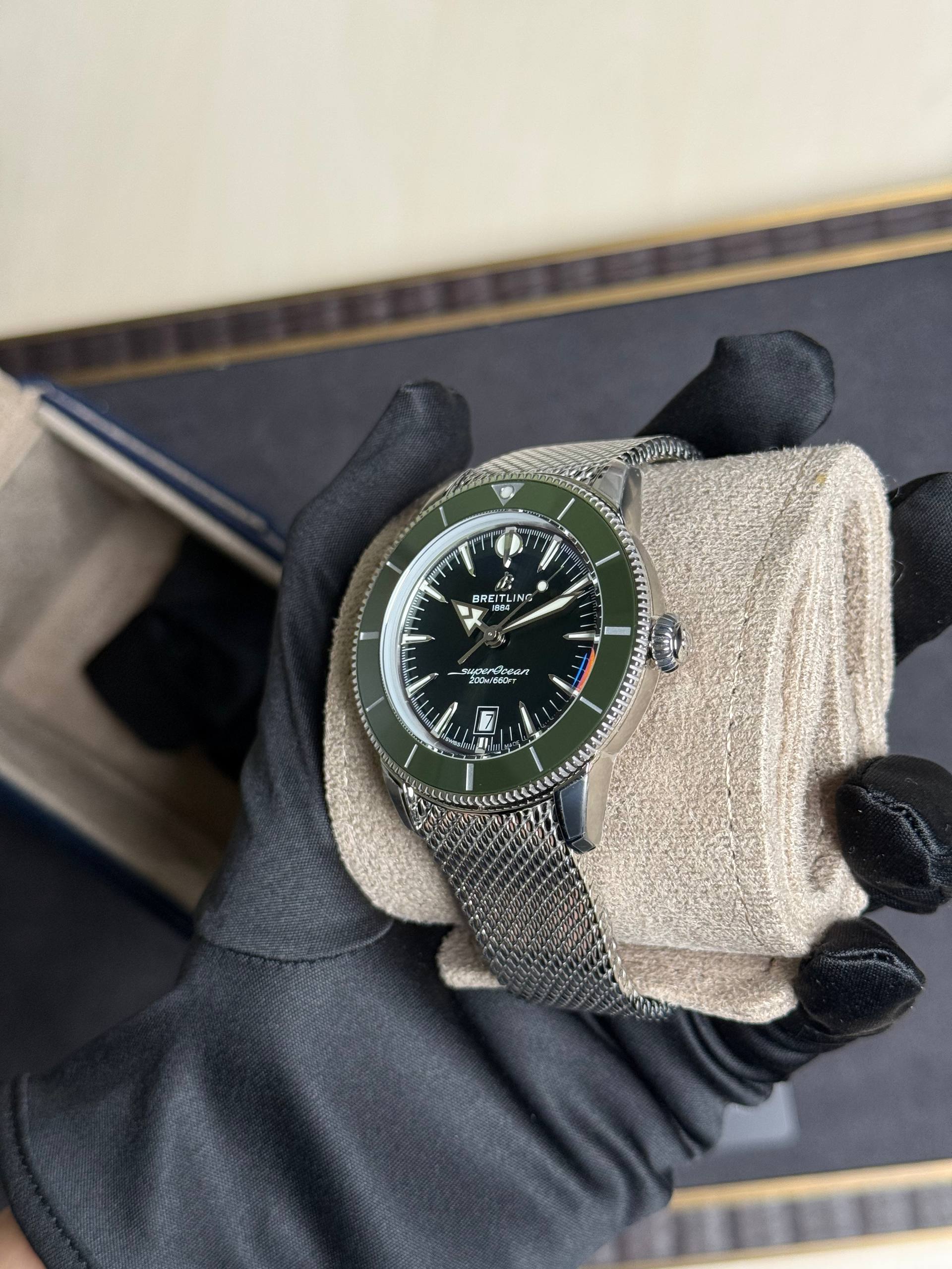 Close-up of a stainless steel Breitling Superocean wristwatch with a green bezel, held by gloved hand.