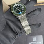 Breitling Superocean wristwatch with a green bezel held by a gloved hand, metal mesh bracelet visible