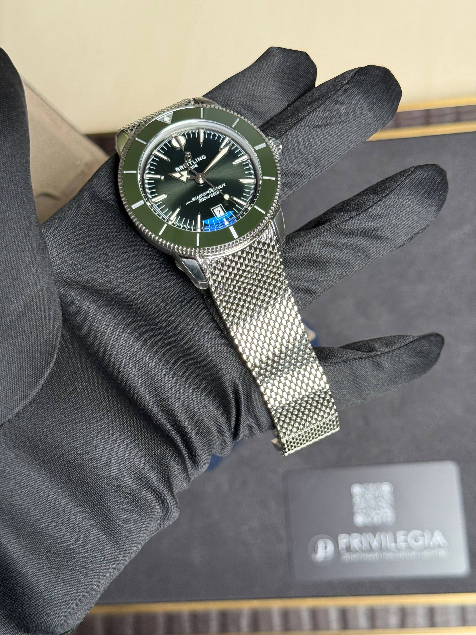 Breitling Superocean wristwatch with a green bezel held by a gloved hand, metal mesh bracelet visible