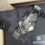 Close-up of a Breitling watch with a metal mesh bracelet on a gloved wrist, showing the clasp and logo text.