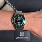 Wristwatch with a green bezel and metal mesh strap on the wrist (Breitling SuperOcean).