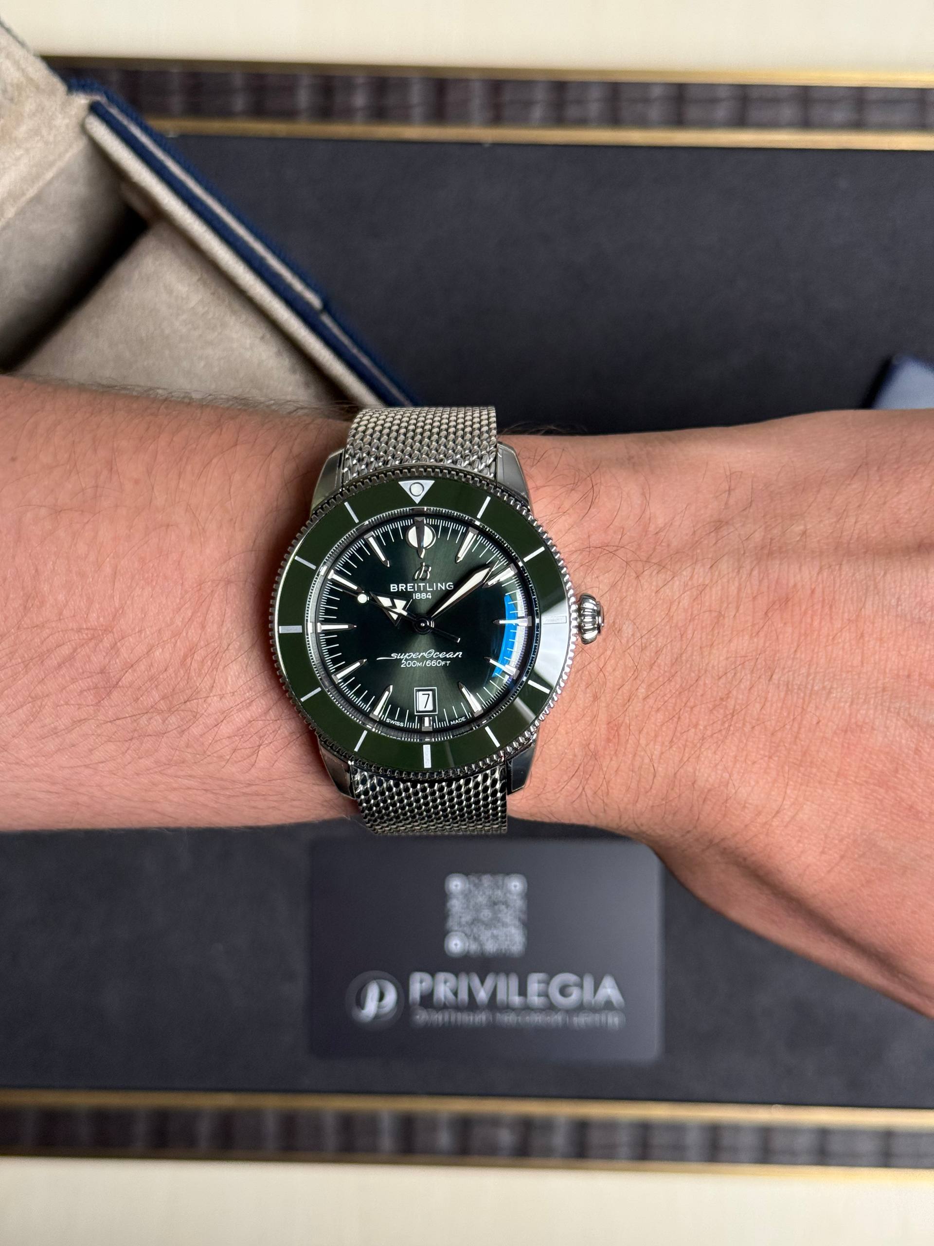 Wristwatch with a green bezel and metal mesh strap on the wrist (Breitling SuperOcean).