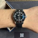 Close-up of a man's wrist wearing a black Breitling SuperOcean watch with a metal mesh band.