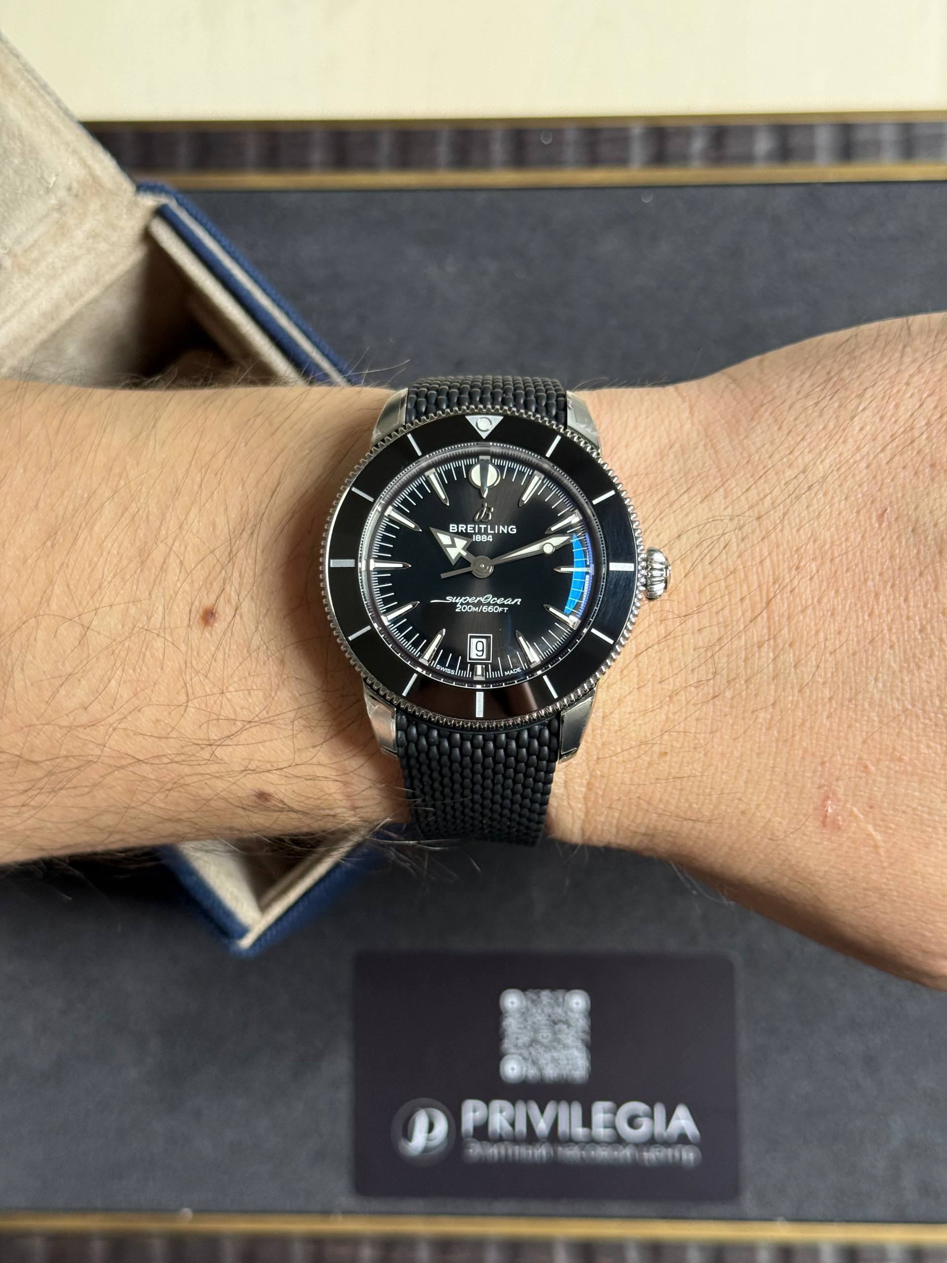 Close-up of a man's wrist wearing a black Breitling SuperOcean watch with a metal mesh band.