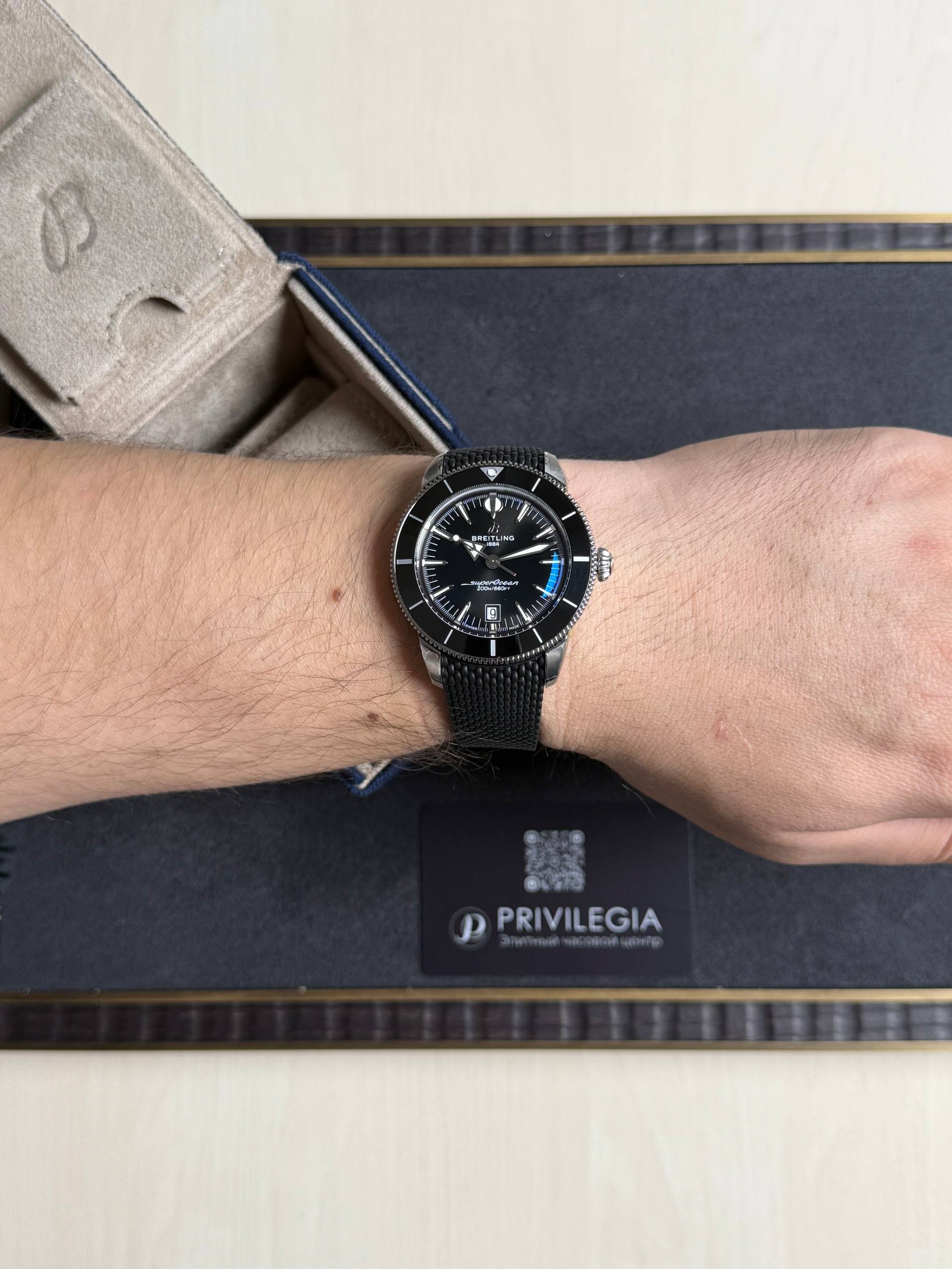 Close-up of a Breitling diver's watch on a forearm, featuring a black dial, silver bezel, and black textured strap.