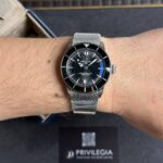 Wrist wearing a Breitling SuperOcean diver's watch with a black dial and silver mesh bracelet.