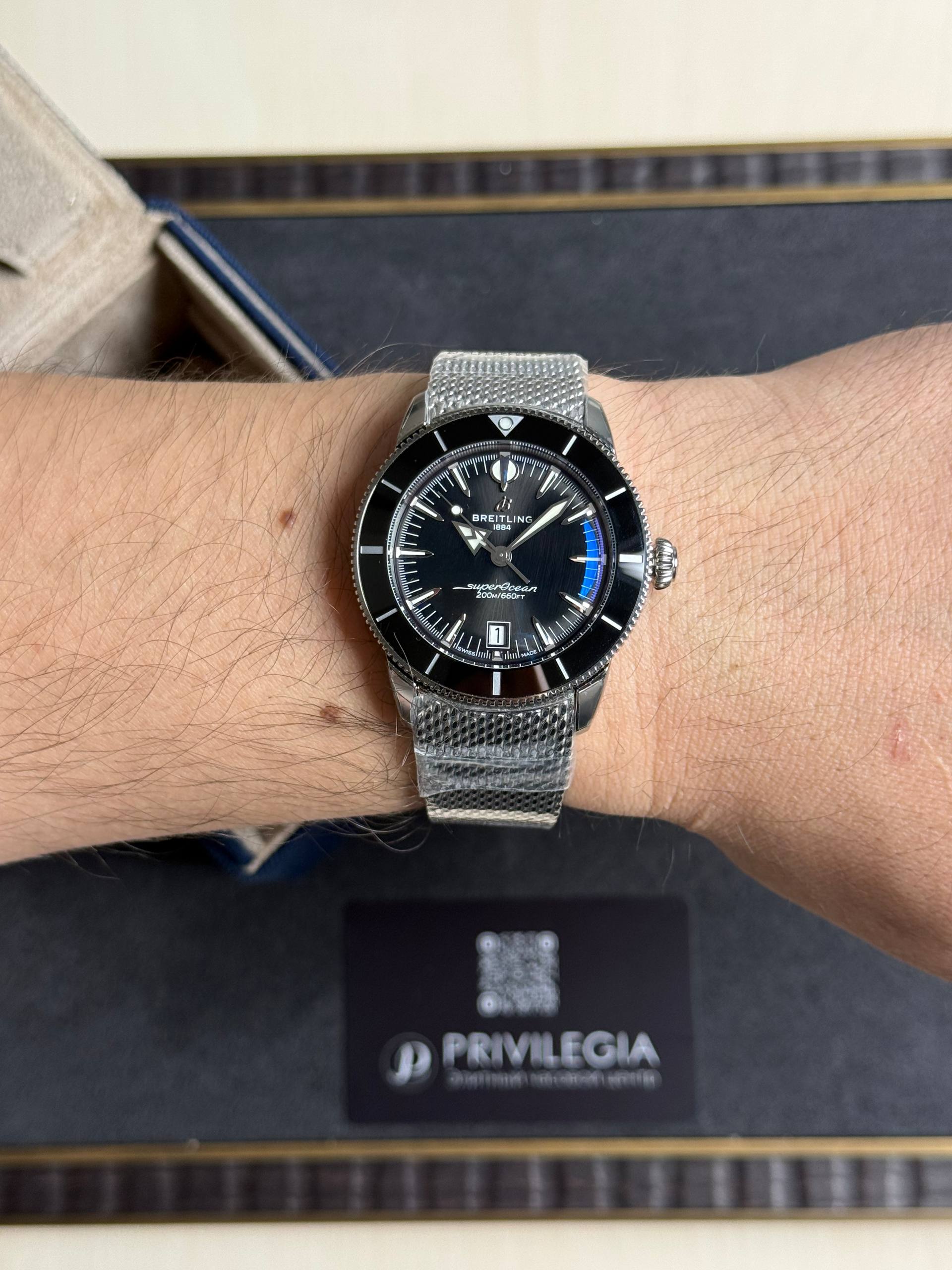 Wrist wearing a Breitling SuperOcean diver's watch with a black dial and silver mesh bracelet.