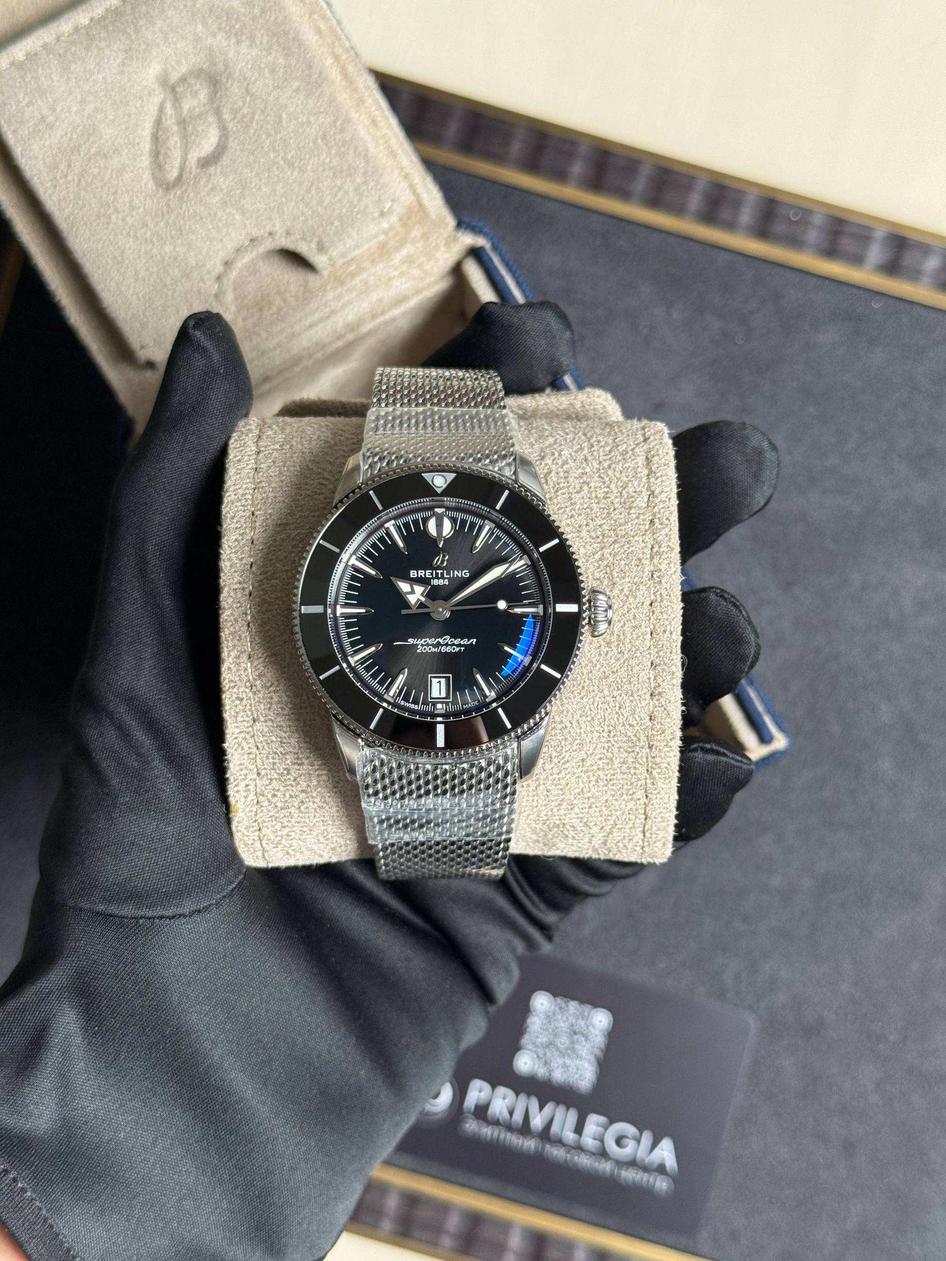 Breitling Superocean wristwatch with a metal mesh bracelet displayed on a beige suede cushion