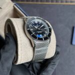 Breitling SuperOcean wristwatch with black dial, silver bezel, and mesh bracelet resting on a beige cushion in a gloved hand.