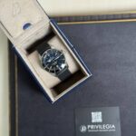 Blue wristwatch with a dark dial and date window nestled in a beige-lined presentation box with a blue exterior strap.