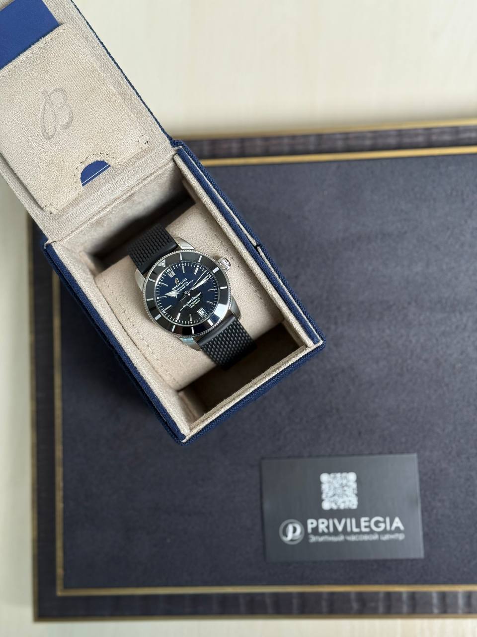 Blue wristwatch with a dark dial and date window nestled in a beige-lined presentation box with a blue exterior strap.