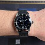 Close-up of a men's Breitling wristwatch with a black dial and metal mesh strap on a light-skinned wrist.