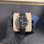 Breitling Superocean automatic wristwatch with black dial and bezel on a beige display cushion, held by a gloved hand.