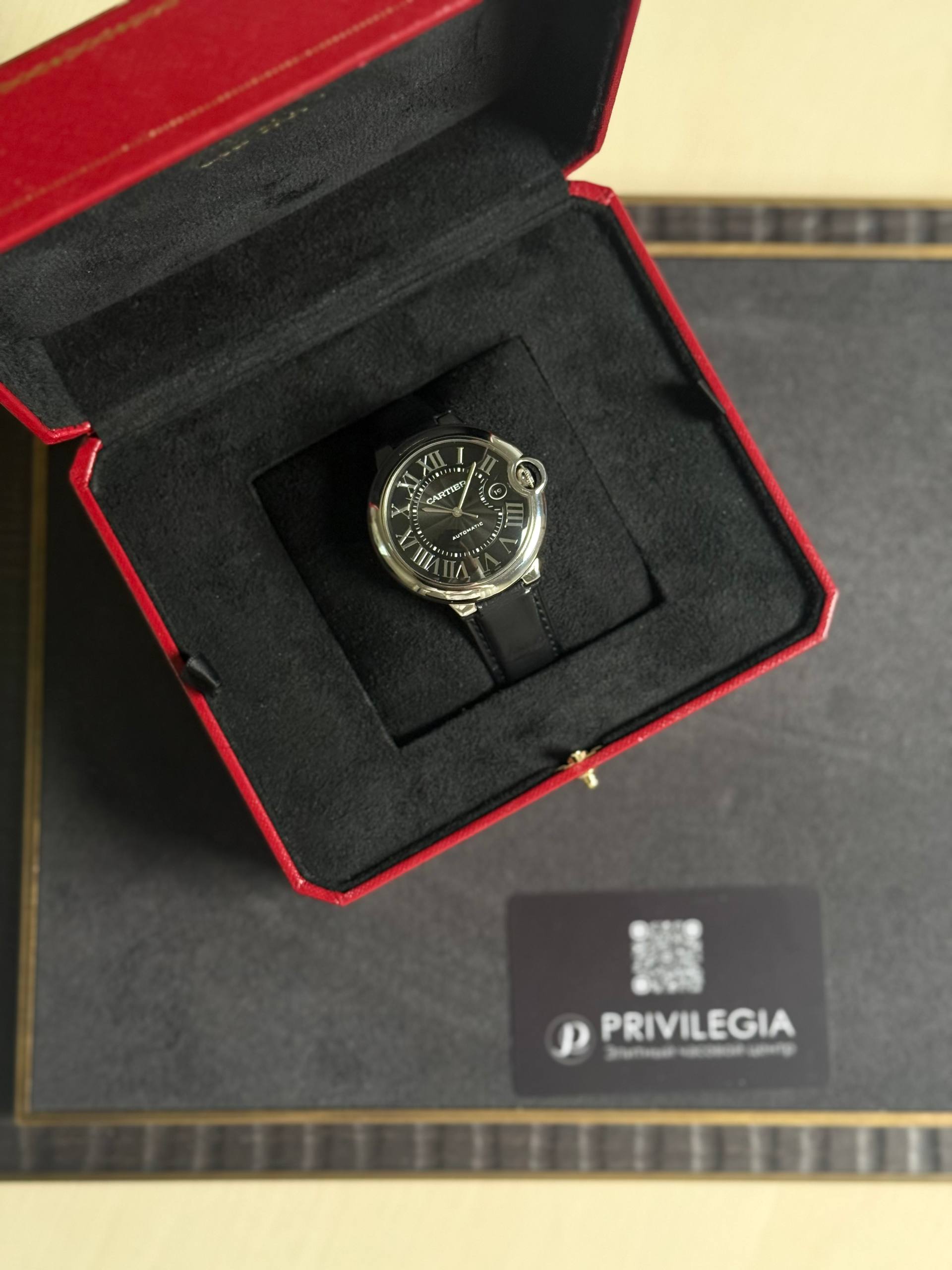 Cartier wristwatch in an open red presentation box with a black interior, showing a black dial with Roman numerals