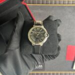 Cartier automatic wristwatch with a black dial and Roman numerals held by a gloved hand.
