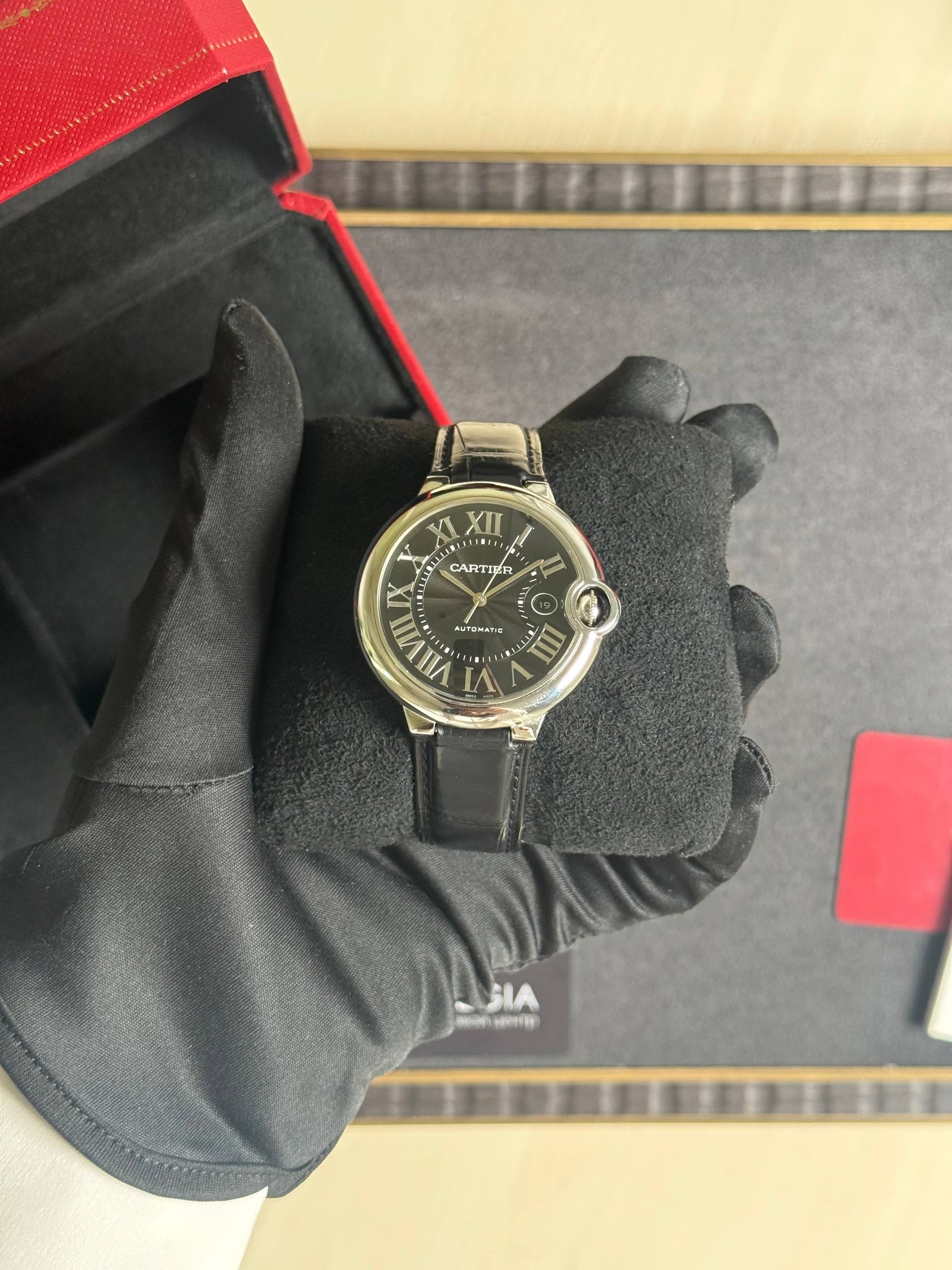 Cartier automatic wristwatch with a black dial and Roman numerals held by a gloved hand.