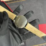 Close-up of a Cartier wristwatch with a beige leather strap, held by a gloved hand; focus on the case back.
