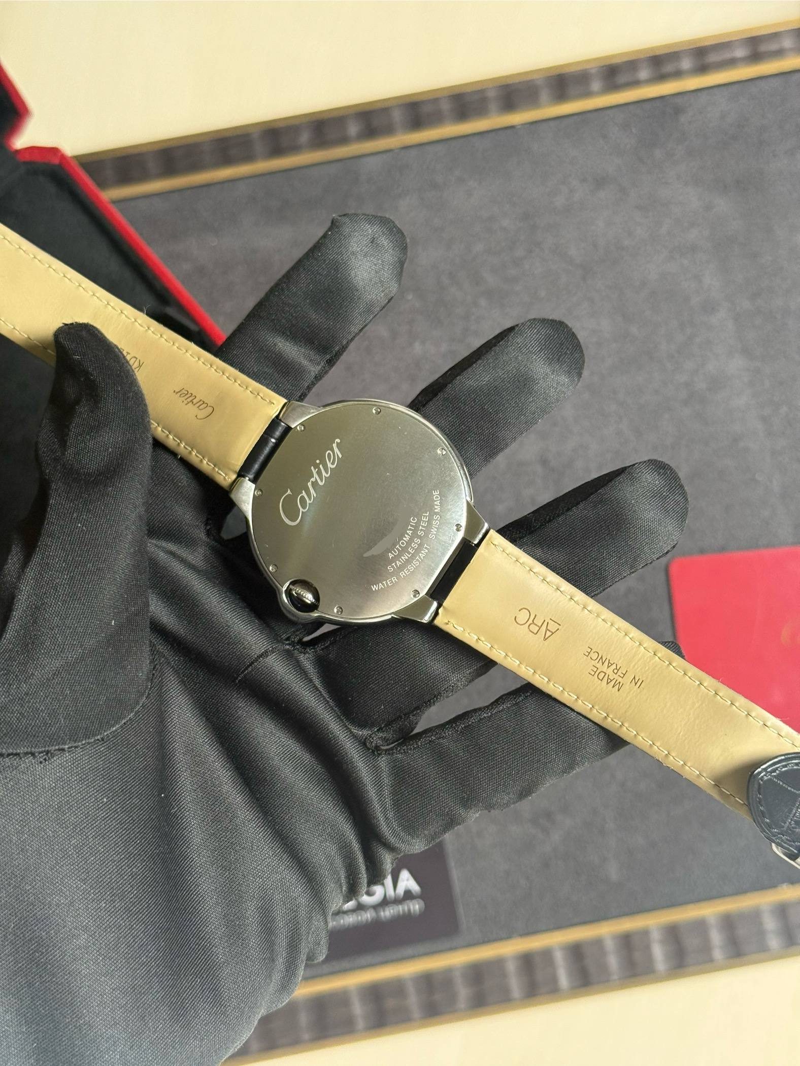 Close-up of a Cartier wristwatch with a beige leather strap, held by a gloved hand; focus on the case back.