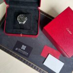 Cartier wristwatch in black dial with Roman numerals in an open red presentation box.