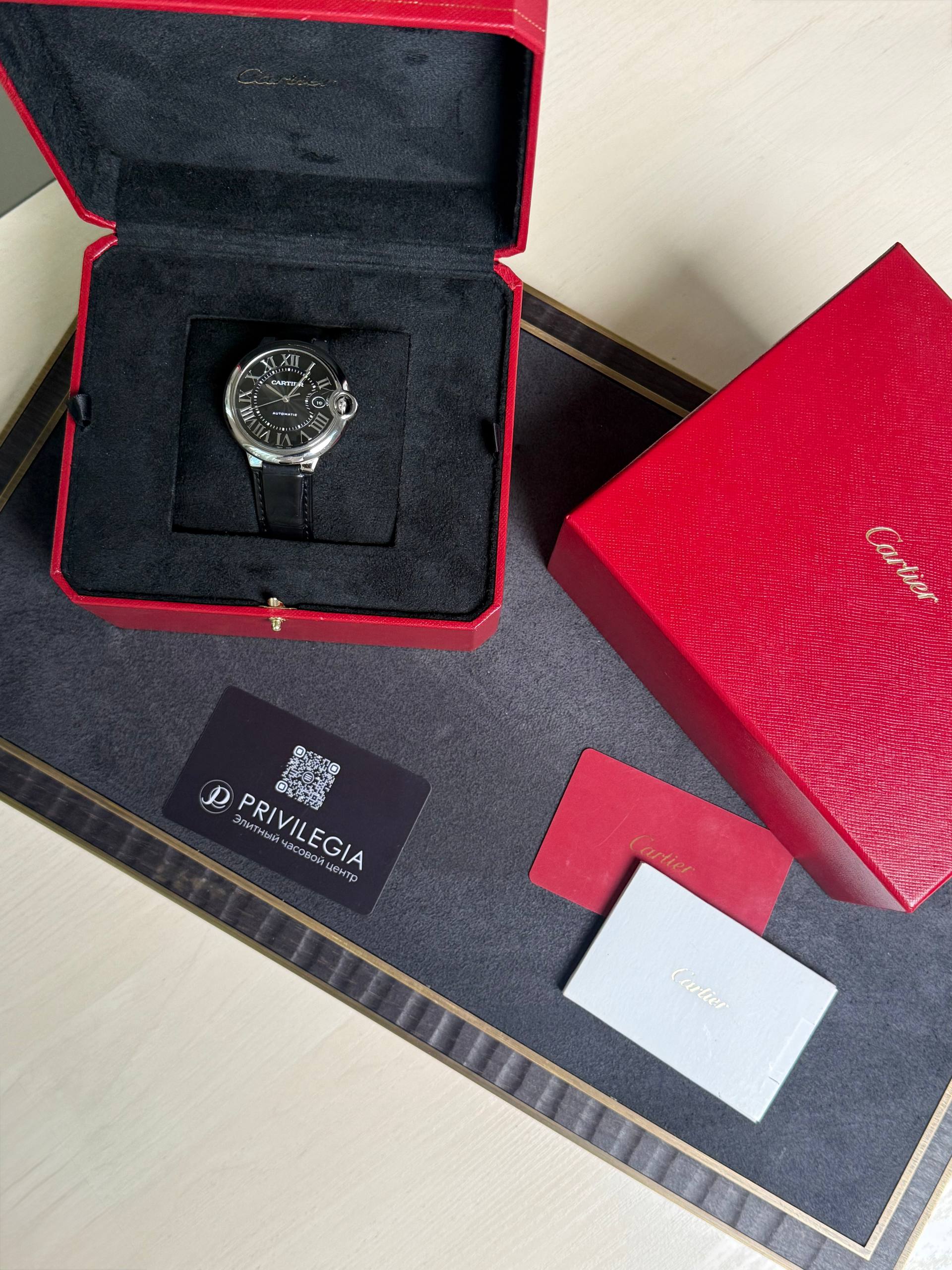 Cartier wristwatch in black dial with Roman numerals in an open red presentation box.
