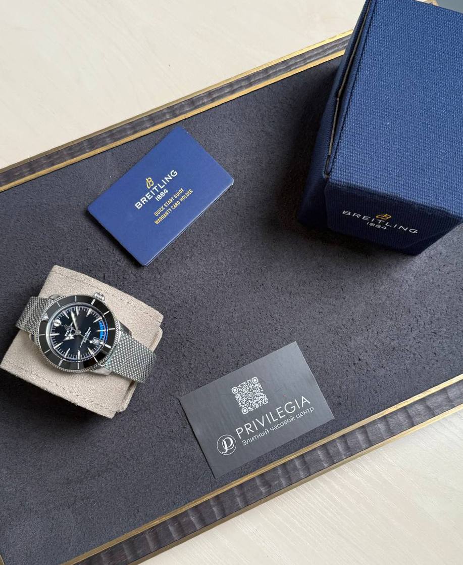 Luxury Breitling watch with metal mesh band displayed on a cushioned stand beside a blue box and business card—watch presentation set.",