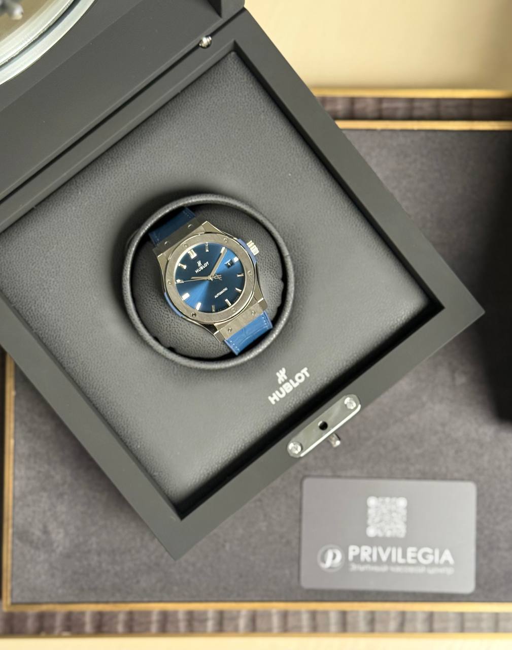 Hublot wristwatch with a blue strap sitting in a black display box with the brand logo nearby.