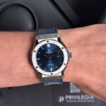 Hublot automatic wristwatch with blue sunburst dial, date window, silver bezel, and blue strap on the wrist.